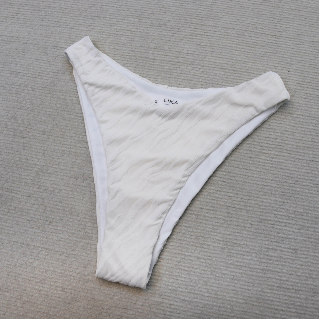 חלק תחתון בגד ים לבן על רקע אפור, בסגנון Lika Swimwear.