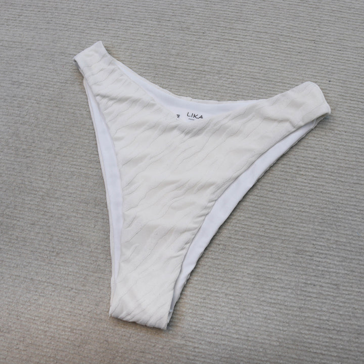 חלק תחתון בגד ים לבן על רקע אפור, בסגנון Lika Swimwear.