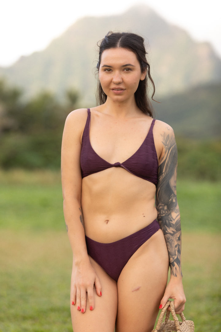 אישה לובשת בגד ים עליון סגול של LIKA Swimwear בחוץ.