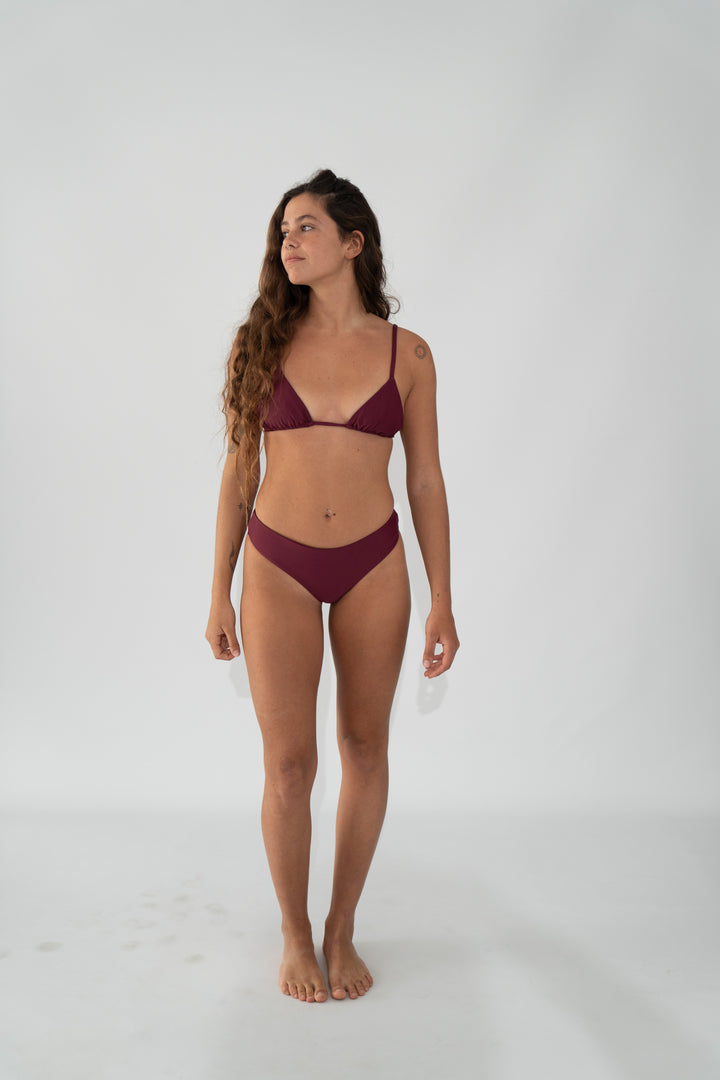אישה לובשת סט בגד ים בצבע בורדו של LIKA Swimwear על רקע חלק.