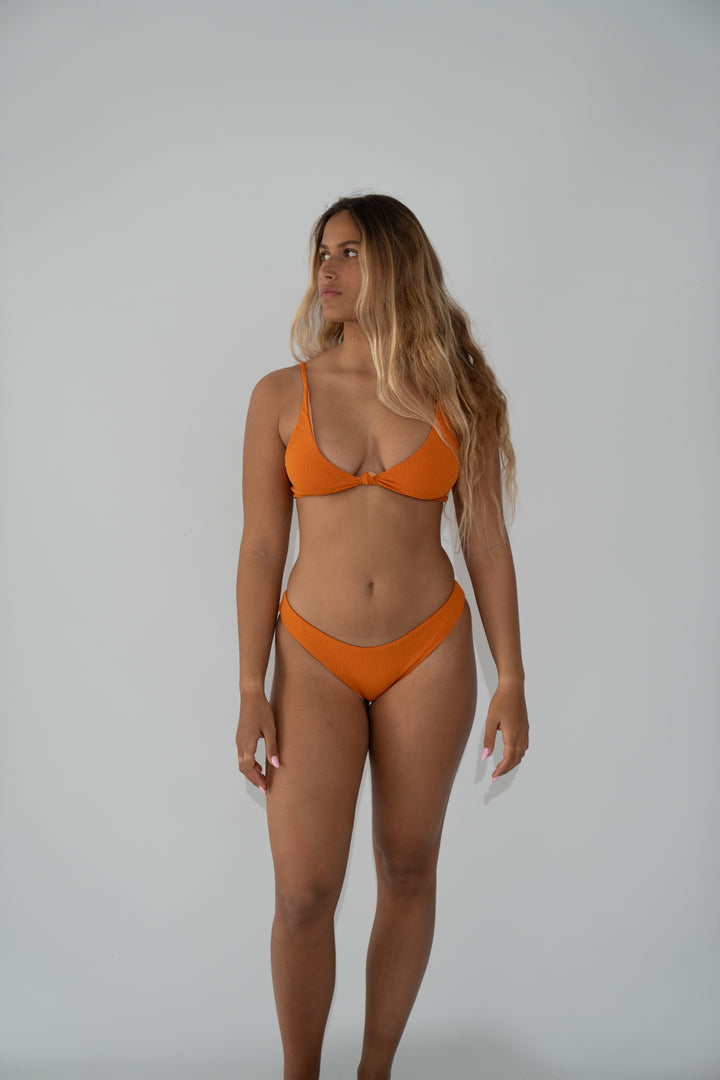אישה לובשת בגד ים כתום של LIKA Swimwear, עומדת על רקע חלק.