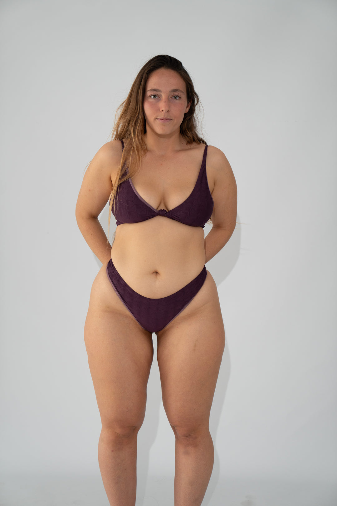 מודליסטית לובשת בגד ים סגול של LIKA Swimwear, עומדת על רקע לבן.
