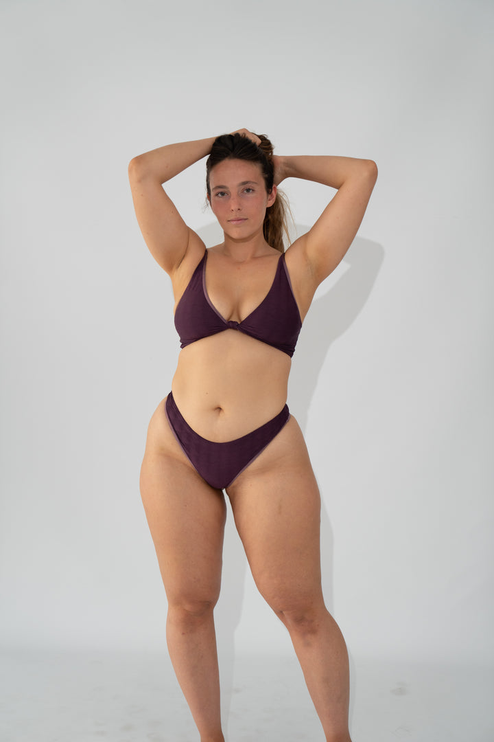 מודליסטית לובשת בגד ים סגול של LIKA Swimwear, עומדת על רקע לבן.